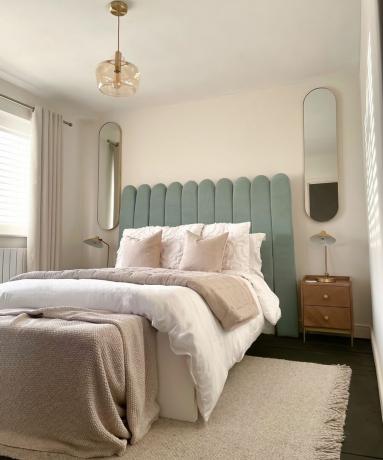 Ein letztes „Nachher“-Bild eines DIY-gepolsterten Kopfteils mit Wellenschliff im Schlafzimmer mit länglichem Spiegeldekor auf beiden Seiten des Bettes, Beistelltischen, Vorhängen und einem cremefarbenen Teppich