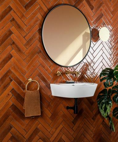 Ochro spalvos plytelėmis išklotas vonios kambarys su baltu kriaukle ir apvaliu veidrodžiu prie sienų ir grindų
