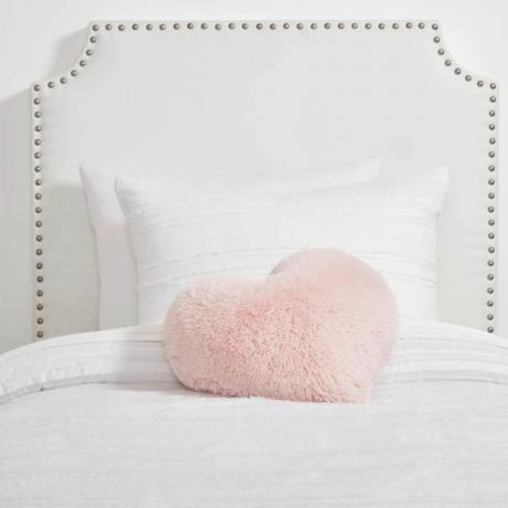Una cabecera blanca con ropa de cama blanca y una almohada rosa.