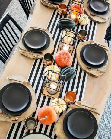 Table en bois clair avec chemin à rayures noires et blanches et citrouilles