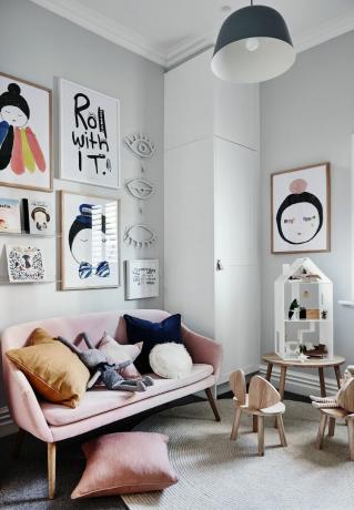 Divertida pared de galería en una pequeña sala de estar con sofá rosa, surtido de cojines negros y mostaza