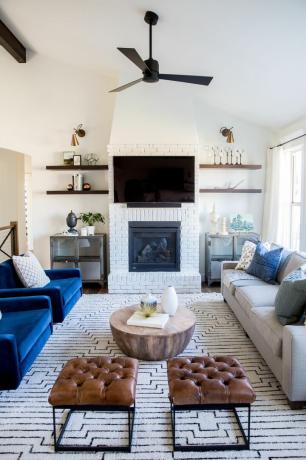 青いソファ、模様入りの敷物、革製のフットスツール、テレビの両側に棚が付いたリビングルーム