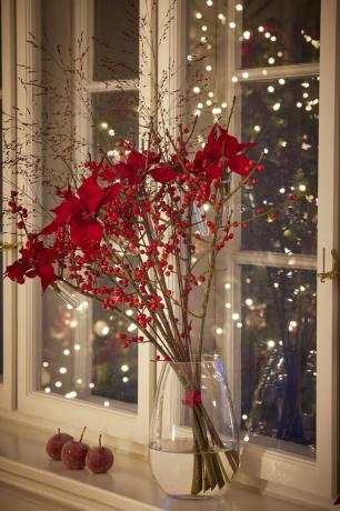 مزهرية زجاجية بها زهور حمراء على حافة نافذة بجوار النافذة