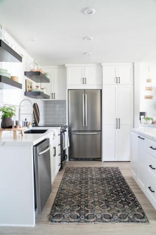 väike köök kambüüsi paigutuses valgete kappide, puitpõrandate, suure Ameerika stiilis külmkapi ja antiikstiilis vaipaga