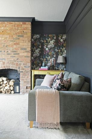 Svartmalt stue med lyst beige gulv, grå sofa, tapetserte alkover og murt peisvegg