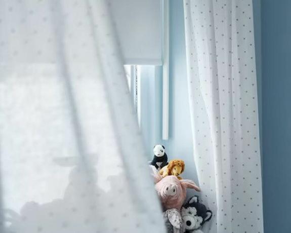 Mėlyname vaikų kambario vėjyje pučiančios baltos užuolaidos