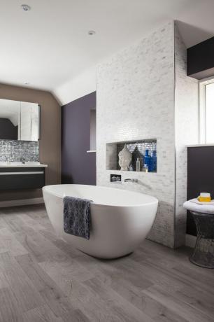 bagno con moderna vasca da bagno indipendente, parete caratteristica piastrellata e pavimento in legno