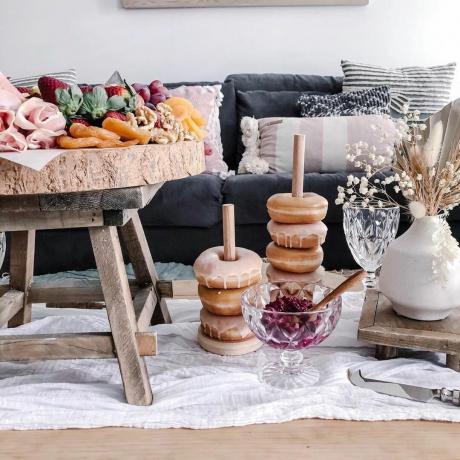 Çörek yığınları ve nefis ikramlarla dolu rustik ahşap masa ve yerde kuru çiçeklerle oturma odası pikniği.