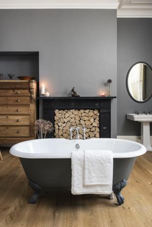 красивая стоячая ванна в центре ванной комнаты с большим камином, заполненным рублеными бревнами