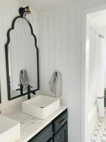 Bílá koupelna pro hosty s obložením stěn a odpovídajícími černými zrcadly