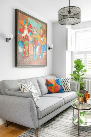Wohnzimmer mit weißen Wänden, grauem Stoffsofa, schwarzer geometrischer Deckenleuchte und farbenfrohen Statement-Kunstwerken