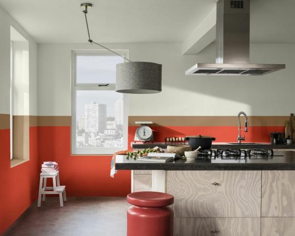 Une cuisine avec un décor mural de couleur rouge et marron avec un îlot au centre de la cuisine, un tabouret rouge et une suspension grise au plafond