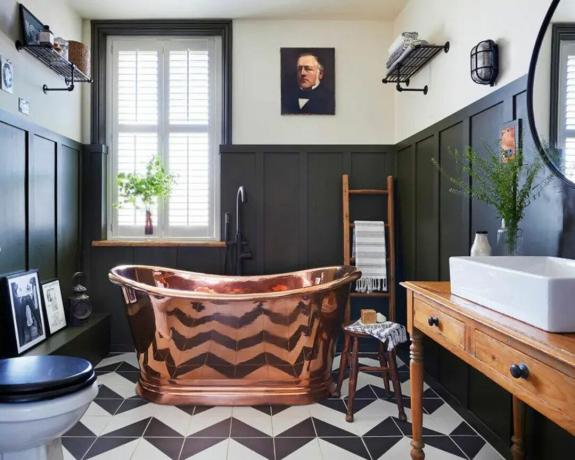 Un baño con bañera de cobre, suelo de chevron y arte mural.