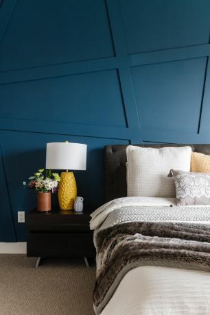 niebieska sypialnia z nowoczesną boazerią, brązowe łóżko, brązowy stolik, żółta lampa, neutralna pościel