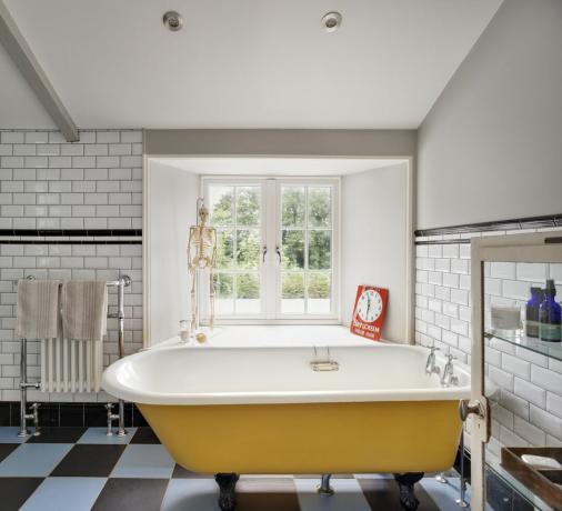 Bak mandi berdiri bebas kuning di kamar mandi putih dengan lantai keramik biru dan hitam