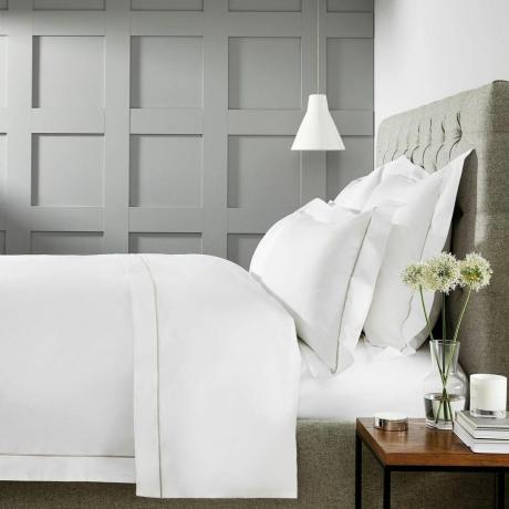 Luksuzna posteljnina na postelji z rastlino na nočni omarici
