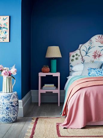パステルカラーのベッドカバーと布張りのベッドフレームを備えた青いコバルトの寝室の壁