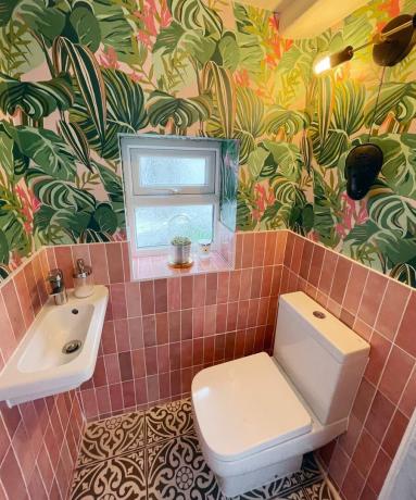 Туалет на нижнем этаже, выложенный розовой плиткой, с обоями с принтом пальм и мозаичной плиткой