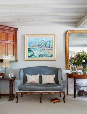 fløyelssofa i stuen med antikke tremøbler og speil og kunstverk