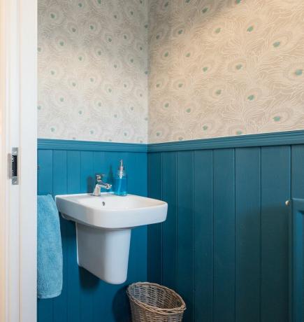 Un piccolo bagno con pareti blu pavone e carta da parati con piume di pavone e niente sulle pareti