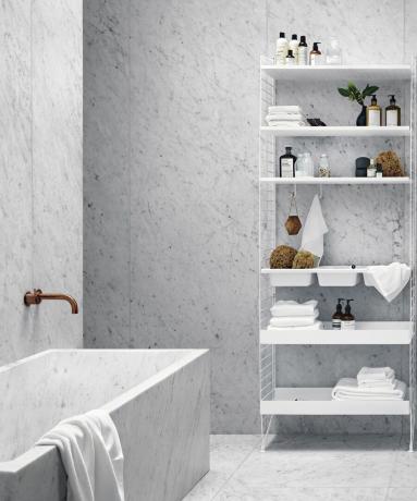 Fehér fürdőszoba káddal, sárgaréz csapteleppel és moduláris polcokkal