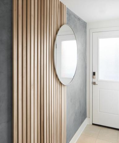 Ξύλινη επένδυση τοίχου από πηχάκι στην είσοδο με στρογγυλό καθρέφτη κρεμασμένο σε γκρι βαμμένο τοίχο