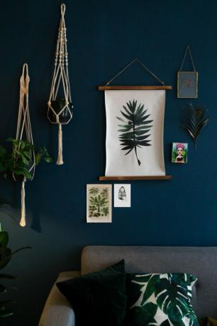 Parete dipinta blu scuro con piante pendenti in macramè e stampe su tela in tessuto