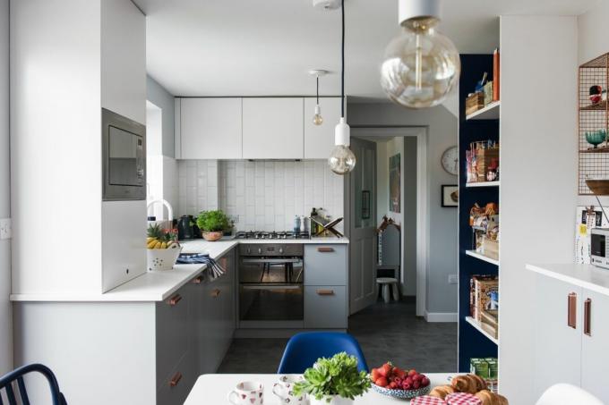 Küche Georgia Broome: Moderne Küche in Grau und Weiß mit monochromen Pendelleuchten, Rückwand aus weißen Metrofliesen und grauem Boden in Schieferoptik