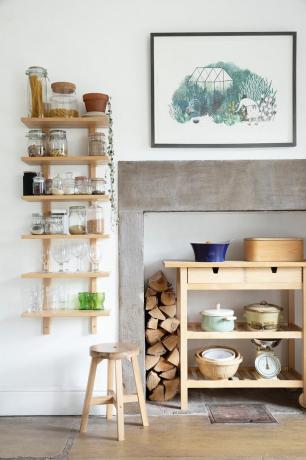 Balta virtuvė su akmeniniu židiniu, medinėmis atviromis lentynomis stiklainiams ir dubenims