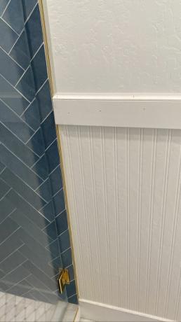 Papel pintado de beadboard blanco instalado en el baño junto a la pared de azulejos azules