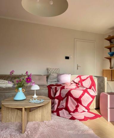 Ένα σαλόνι με ένα ροζ και κόκκινο ριχτάρι σε έναν καφέ καναπέ και ένα κυκλικό τραπεζάκι