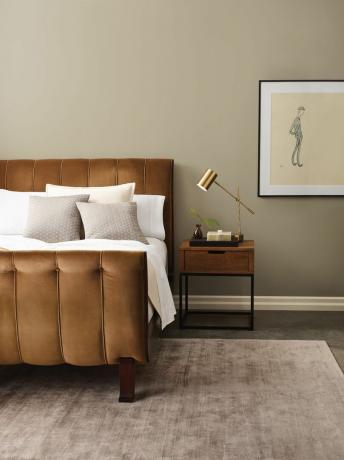 Schlafzimmer mit Steinwänden, gepolstertem Bett, Beistelltisch, taupefarbenem Teppich, Kunstwerk, Tischlampe aus Messing