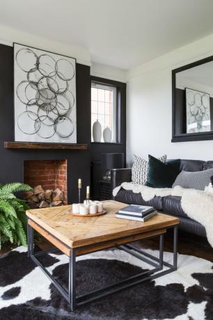 Ein schwarz-weißes Wohnzimmer mit Wandkunst in Blasenoptik, einem Teppich mit Kuhmotiv, einem stillgelegten Kamin und einem großen Spiegel mit schwarzem Rahmen