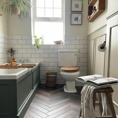 łazienka z zielonoszarą wanną, błyszczącymi płytkami ściennymi metra, drewnianą podłogą i roślinami