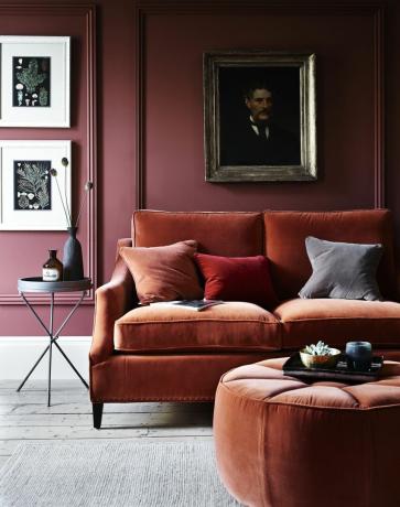 Sofá de terciopelo naranja oscuro en una sala de estar con paredes de color rojo oscuro