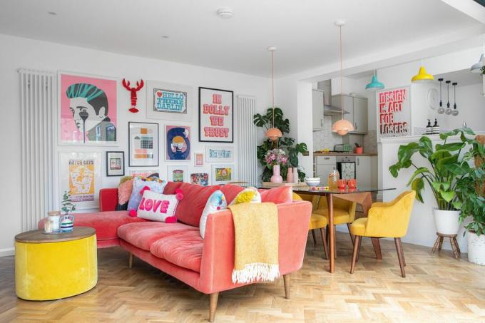 Kleurrijke woonkamer met parketvloer, roze bank, gele eetkamerstoelen en fotowand