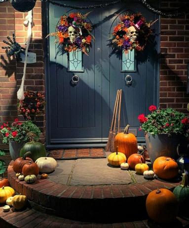 Halloween ajtódíszítési ötletek két koponya ajtókoszorúval és különféle sütőtökökkel a sötétkére festett bejárati ajtón és környékén
