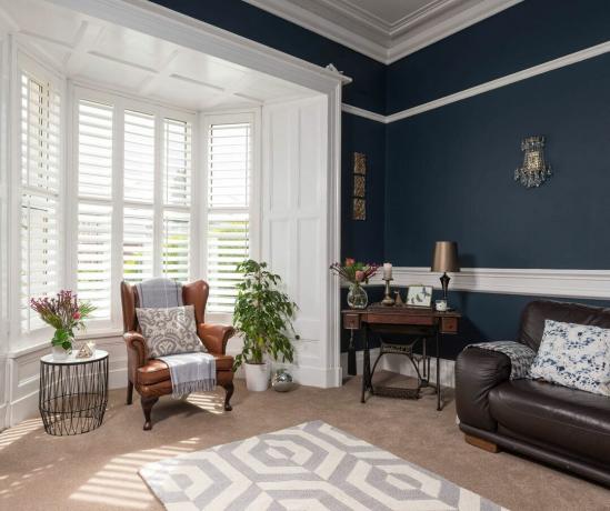 sufragerie cu pereți albaștri, un fotoliu tradițional din piele cu pătură, canapea și covor geometric