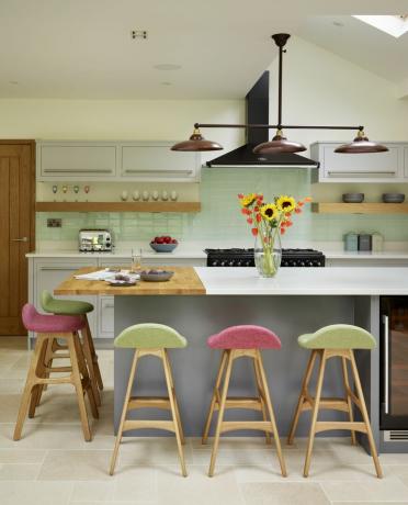 ღია მწვანე ნაკაწრი თეთრ სამზარეულოში დიდი კუნძულით ვარდისფერი და მწვანე ბარის სკამებით