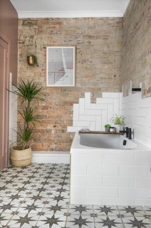 Cuarto de baño con pared de ladrillo, azulejos de metro blancos, baño blanco y suelo de baldosas estampadas