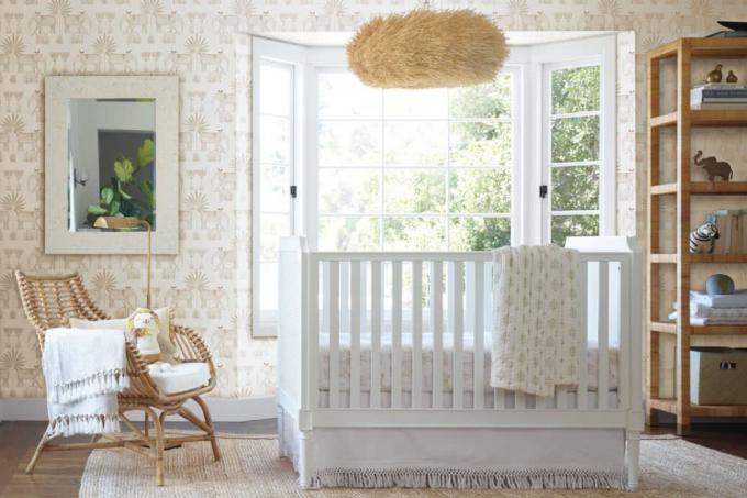 白い木製のベビーベッドと籐のアクセントの椅子と織り目加工の色合いと保育園のニュートラルな壁紙