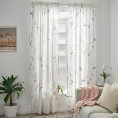 Hvite gardiner i stuen med veggkunst, stueplante og babyrosa kastes over nøytral sofa