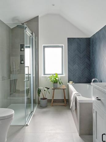Baltas vonios kambarys su pilkomis plytelėmis dušo kabinoje ir mėlynomis ševroninėmis plytelėmis virš vonios