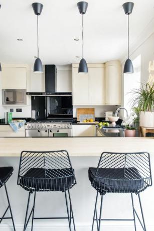 Krémová kuchyňa s barovým pultom, čiernymi kovovými barovými stoličkami a štyrmi čiernymi závesnými svietidlami