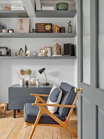Hvid stue med gråmalede åbne hylder og en mid-century lænestol med grå sædehynder