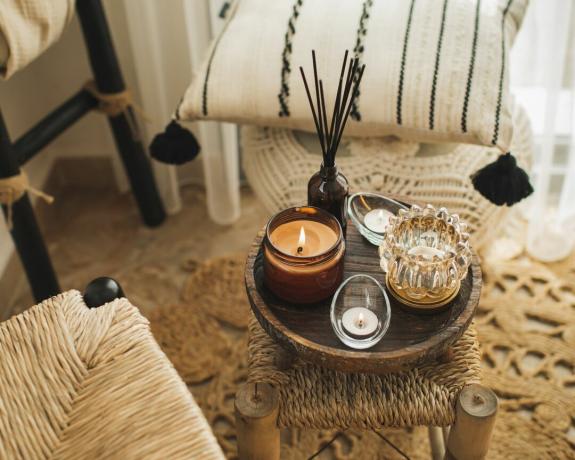 Pinti baldai su ekologiškomis medžiagomis, rankų darbo pagalvėlės, aromatinis nendrių difuzorius, degančios žvakės ir tekstilė boho prašmatniame interjere. Hygge ir aromaterapijos koncepcija. Jaukus žiemos ar rudens metas.