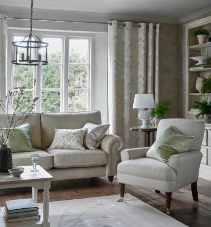 Sala de estar cinza com sofá de dois lugares e cadeira, lustre e abajur de mesa de abacaxi