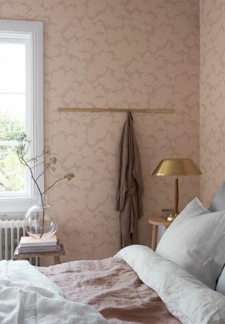 Papel pintado rosa suave para dormitorio de Boras Tapeter con detalles dorados y ropa de cama de lino blanco