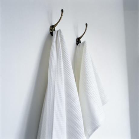 witte badhanddoeken op koperen haken en een witte muur