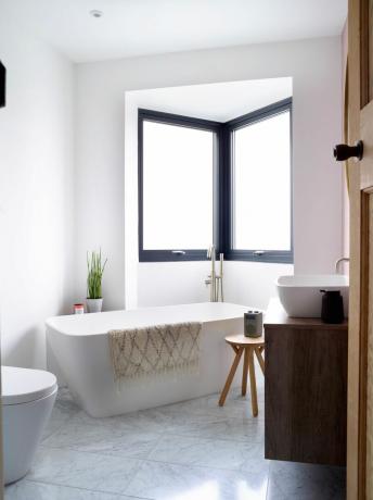 moderni kylpyhuone, jossa on vapaasti seisova kylpyamme, seinälle ripustettavat yksiköt, valkoiset seinät ja puinen pöytä